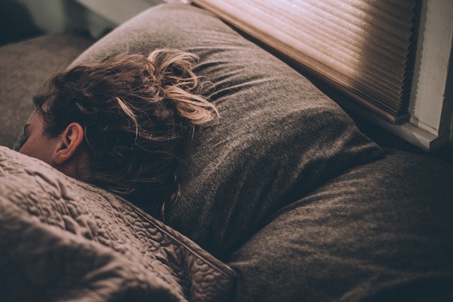 woman sleeping on a bed under brown blankets